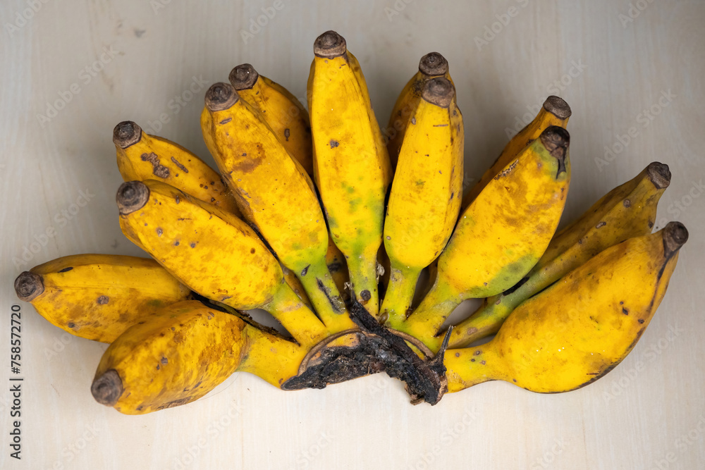 A bunch of yellow ripe bananas on a wooden background. Bananas are a nutritious fruit that has many health benefits. - obrazy, fototapety, plakaty 