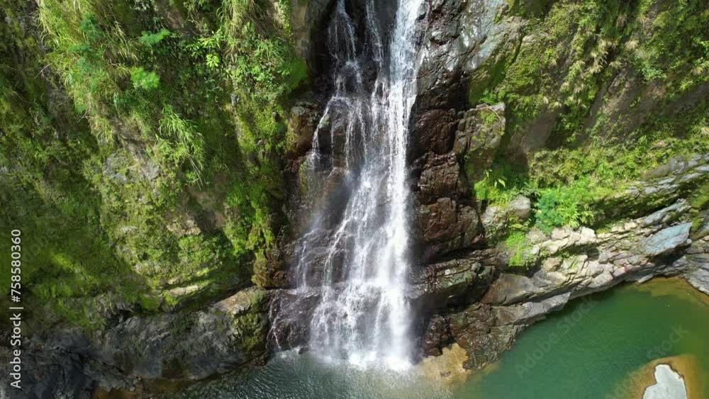 Cinematic drone shot of cascading waterfall in tropical landscape of Dominican Republic. Sunny day with mossy rocky cliff face. Aerial tilt up. Cinematic drone shot of cascading waterfall in tropical landscape of Dominican Republic. Sunny day with mossy rocky cliff face. Aerial tilt up.