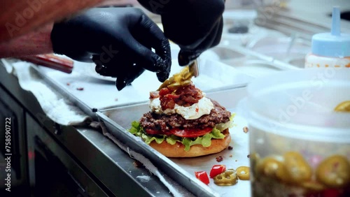 4K Cinematic food cooking footage of a chef preparing and making a delicious homemade burger in a restaurant kitchen in slow motion putting the toppings on top of the smashed burger photo