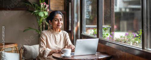 Professional elderly Indian woman with laptop in a modern cafe. Concept to demonstrate active interaction of elderly people with technology and neural networks for work and social connection. © Alisa