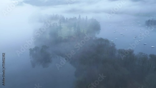 Approaching drone shot of misty island on Bowness-on-Windermere Lake, located in Furness District in Cumbria's Natiional Park in England. photo