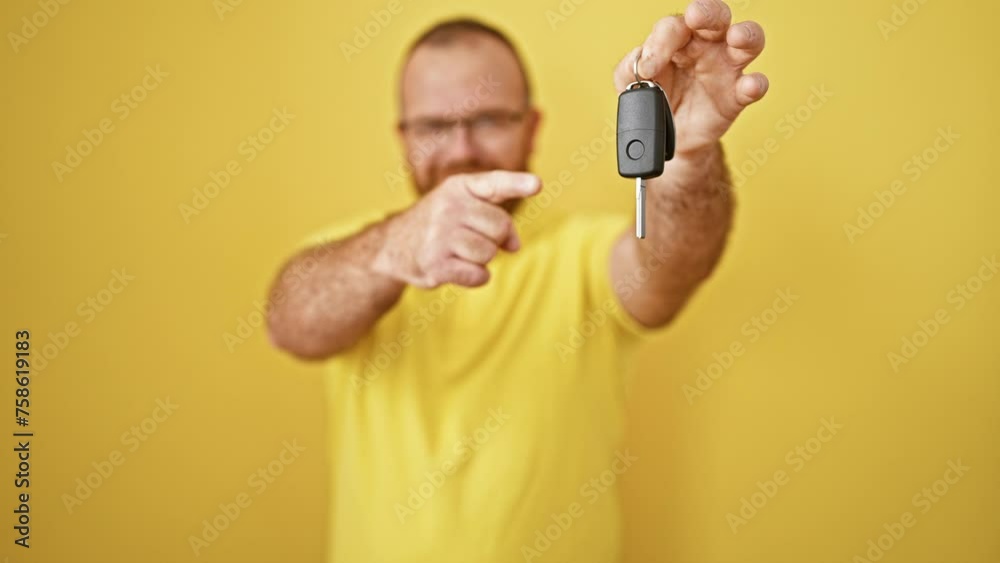 Handsome middle-aged caucasian man, confidently smiling, showing off the key to his new car, joyfully pointing finger, standing against a bright yellow isolated background Handsome middle-aged caucasian man, confidently smiling, showing off the key to his new car, joyfully pointing finger, standing against a bright yellow isolated background