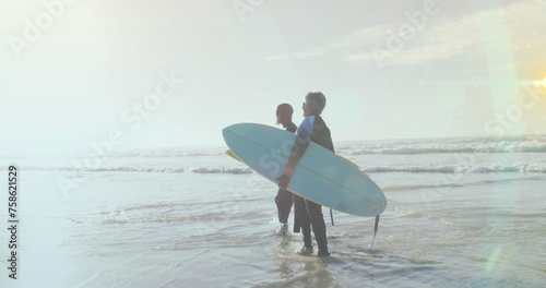 Image of light spots over senior african american couple with surfboards on sunny beach