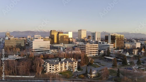 HDR stock drone video of Anchorage city skyline at sunset with warm glow on buildings. Aerial view of Alaskan city moving up and left