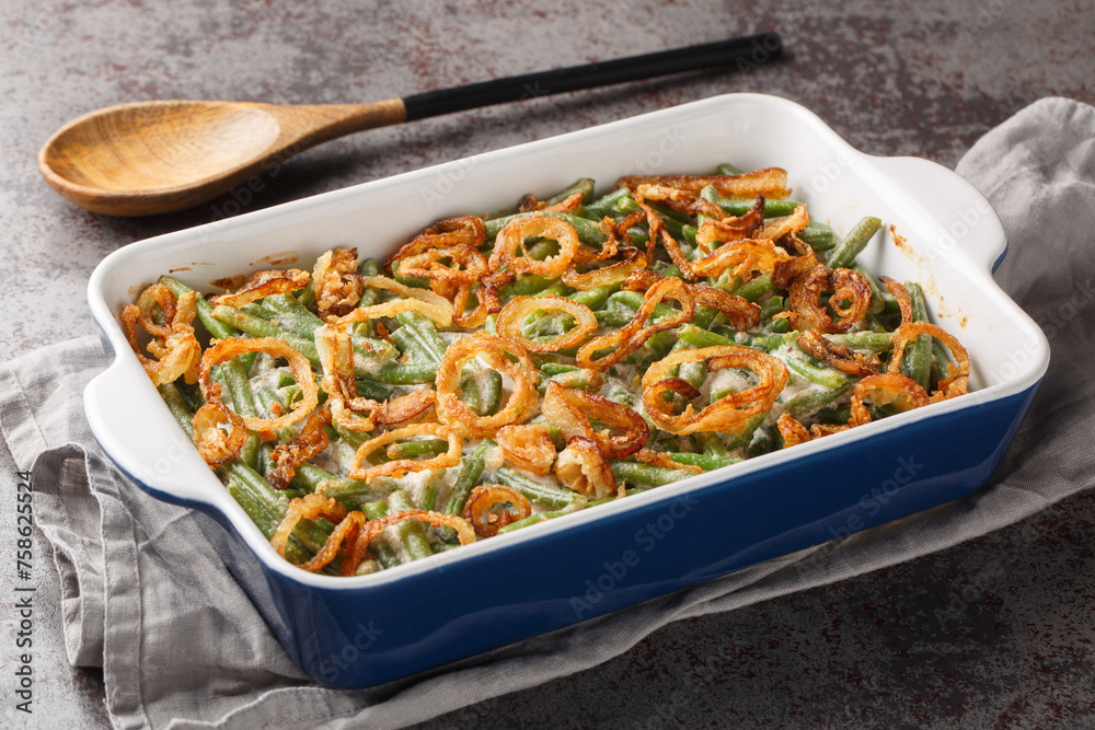 Green bean casserole with cheesy mushroom sauce and topped with crispy onions close-up in a baking dish on the table. horizontal