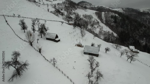 Snowy cindrel mountains with isolated cabins, leafless trees, and winding trails, aerial view photo