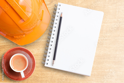 Safety helmet and cup of coffee with notebook on wooden table photo