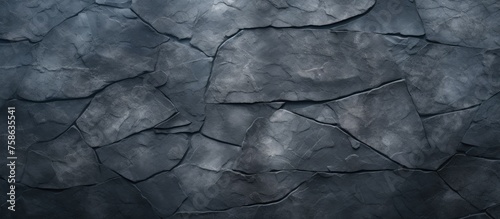 A close up of a grey cracked stone wall with a pattern of tints and shades, resembling monochrome photography. The rock merges with darkness