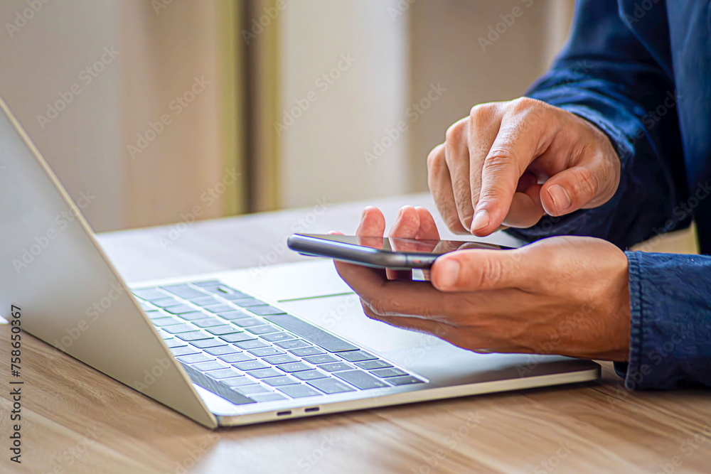 Fototapeta premium Woman working online on the keyboard of her laptop computer While holding the phone