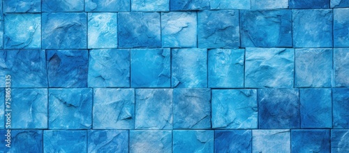A close up of a blue rectangular tile wall with shades of azure and aqua  creating a symmetrical pattern resembling an art piece. The electric blue tints add depth to the flooring design