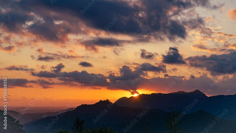 Obraz premium Sunset on a tropical island. The sun illuminates the sky against the background of the silhouette of the mountain and the jungle.