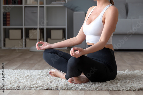 Sporty young woman practicing yoga at home, sitting in lotus pose
