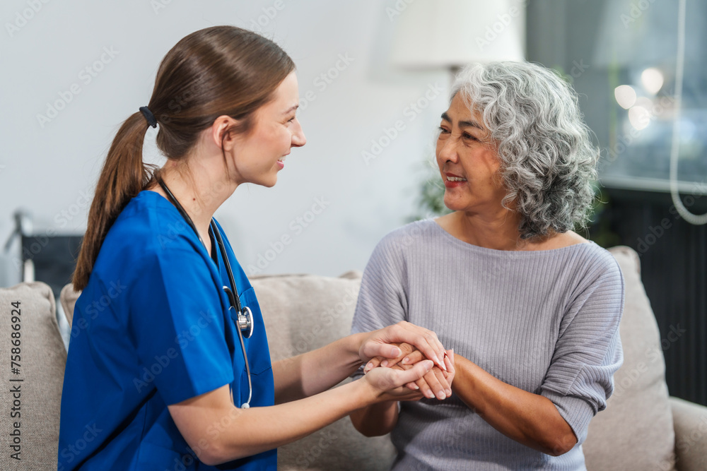 Obraz premium Caucasian female doctor offers encouragement to Asian mature elderly patient woman while holding hands, providing comfort and support during a medical consultation at sofa.