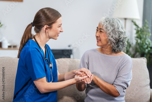 Caucasian female doctor offers encouragement to Asian mature elderly patient woman while holding hands, providing comfort and support during a medical consultation at sofa.