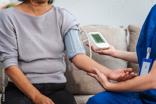 Caucasian female doctor checks health with blood pressure monitor on elderly Asian patient on sofa photo