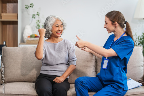 Caucasian female doctor shares a celebratory high five with an elderly Asian patient while both are seated together on the sofa. photo