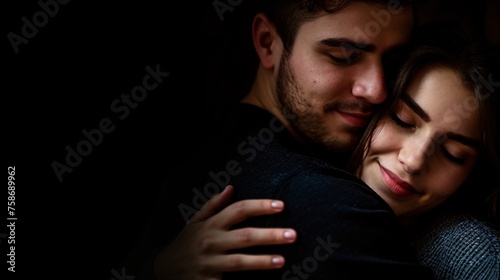 A pair of infatuated individuals embrace on a dark backdrop.