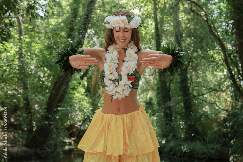Graceful young woman dancing Hawaiian hula in the outdoor jungle scenery. Concept of indigenous Polynesian dances. Sensation of exoticism and mystery. Showing the palms of the hands.
