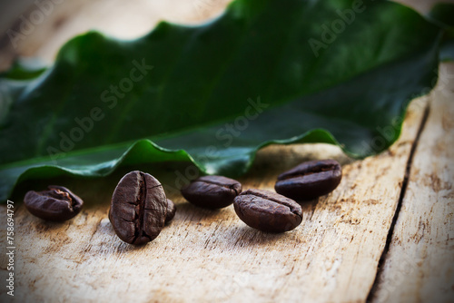 Coffee beans and green leaf on wooden background