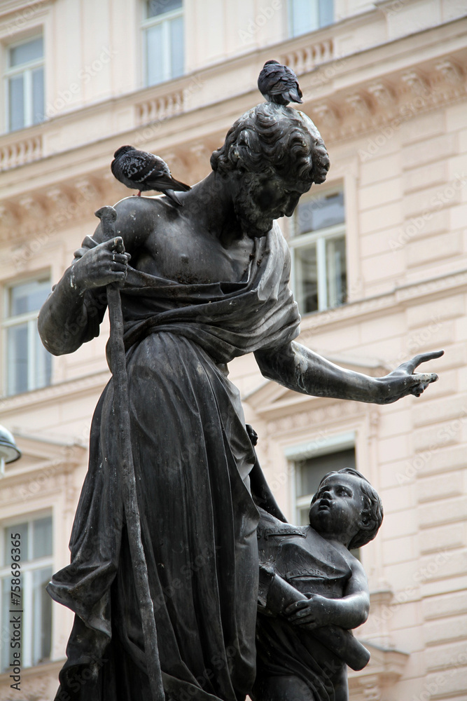 Pigeons on an antique man and child monument with a historic building in the background
