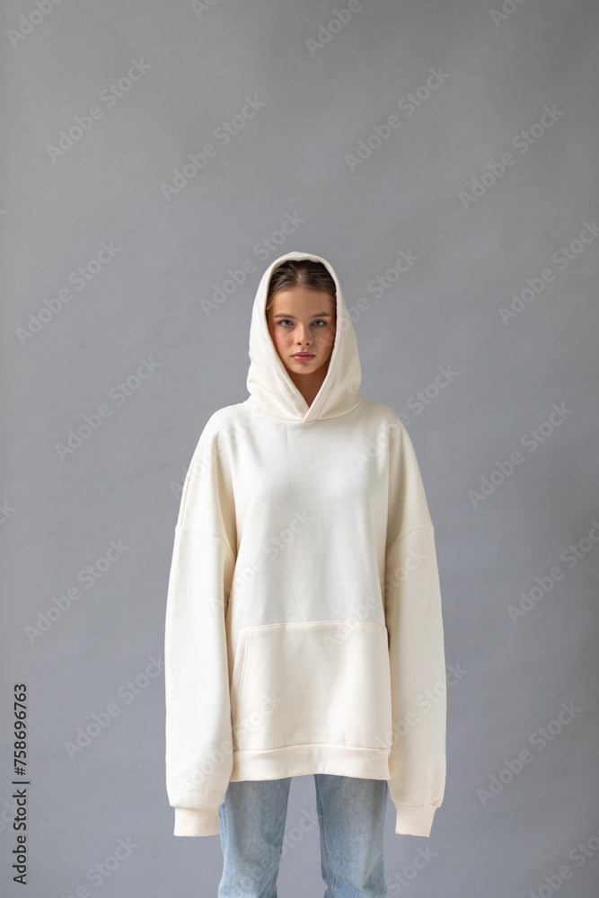 Beautiful blonde woman in a white hoodie and blue jeans posing on a gray background - obrazy, fototapety, plakaty 
