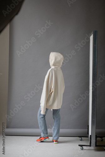 Beautiful blonde woman in a white hoodie and blue jeans posing on a gray background