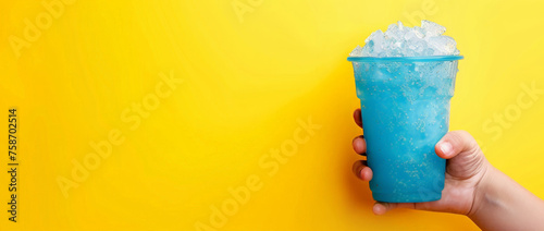 The hand holds a cup with a milk slushie. A  blue glass with a  coconut slushie  on a yellow background, place for text photo