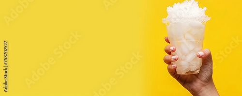 The hand holds a cup with a pineapple  slushie. A glass with a pineapple  slushie  on a yellow background, place for text photo