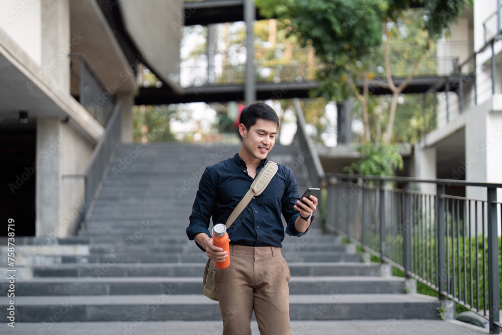 Fototapeta premium Smiling asian businessman walking to work while to hold reusable eco friendly ecological cup in the city