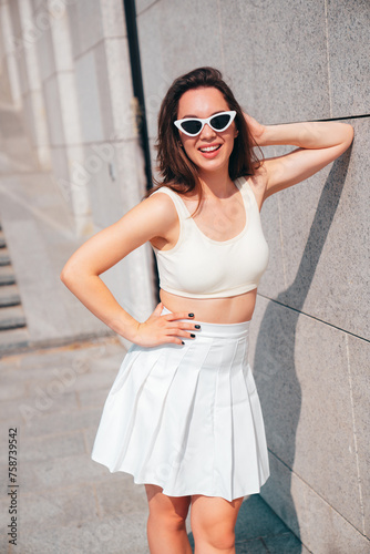 Young beautiful smiling hipster woman in trendy summer white tennis skirt and tank top clothes. Carefree woman posing in street at sunset. Positive model outdoors. Cheerful and happy, in sunglasses