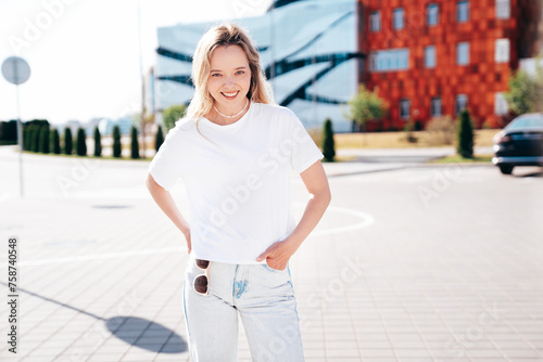 Portrait of beautiful smiling model in sunglasses. Female dressed in summer hipster white T-shirt and jeans. Posing in the street. Funny and positive woman having fun outdoors