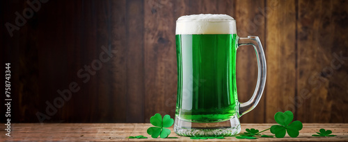 Glass of green ale on wooden table, with blurry green background and clover leaves.