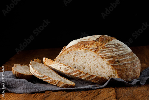 Rustic sourdough bread with cut slices on a wooden table. Panorama, black background with free space for text.	
