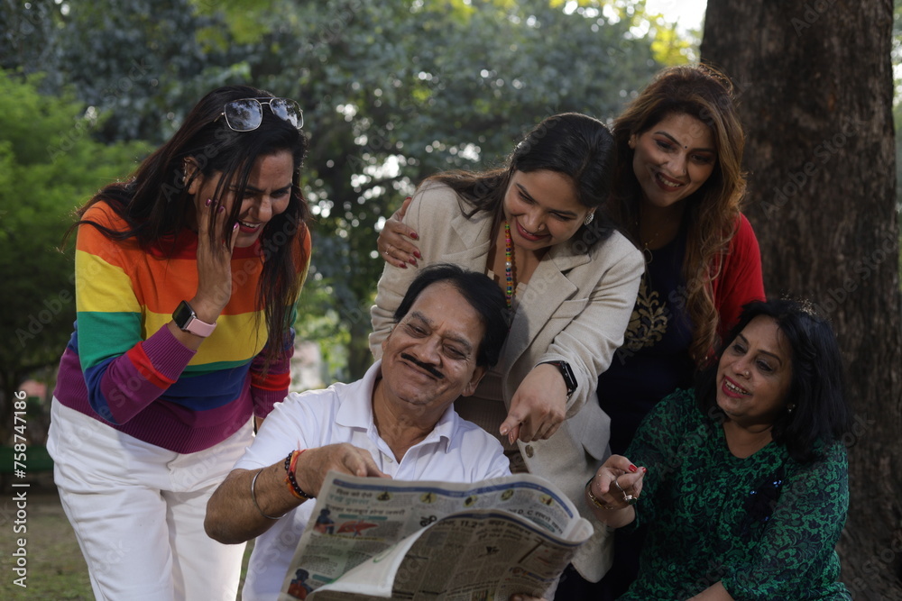 Obraz premium Reunion of happy Indian friends. green park lush green atmosphere. tranquil and serene environment. elderly old friends together. everyone in park reading a newspaper and having fun in day time.