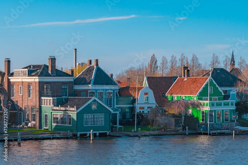 Beautiful Dutch scenery panorama of Zaanse Schans village in Netherlands in spring time. Ancient houses brightly colored at the water's edge against a blue sky in sunny weather