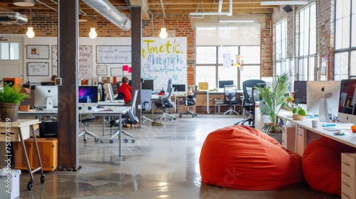 A contemporary office space featuring a large bean bag chair positioned in the center of the room. The office is tidy and minimalist in design, with visible tech gadgets and workstations around the be