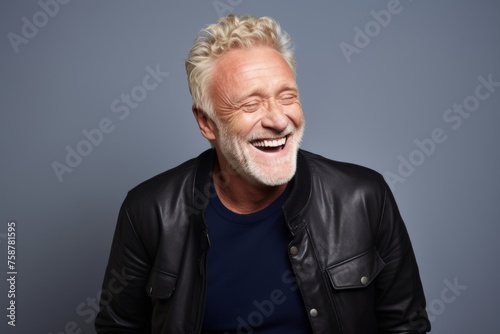 Portrait of a happy senior man laughing against a grey background.