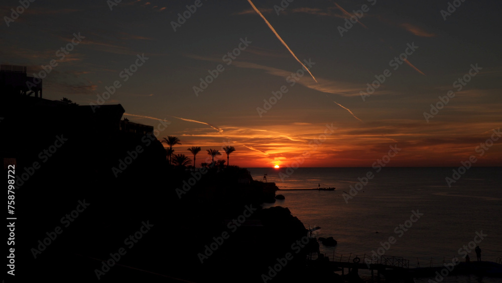 A picturesque sunrise at sea. Silhouettes of palm trees on the shore