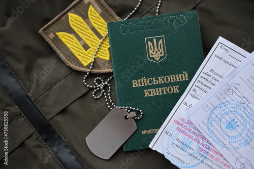 Military token or army ID ticket with mobilization notice lies on green ukrainian military uniform indoors close up photo