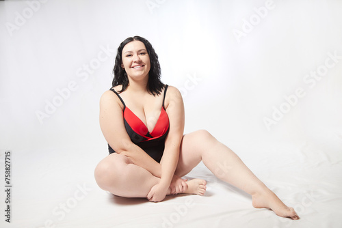 Portrait of attractive dreamy thick woman in red black swimsuit posing on white background. Body positive, photo shoot, selfie. Funny plus size model © keleny