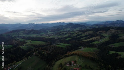 Drone flying around the landscape of Semriach in autumn, with green hills and small houses in the front, mountains in the back photo