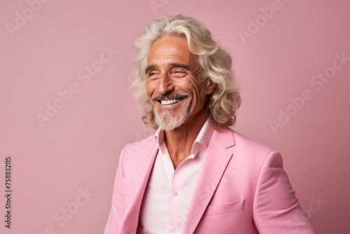 Portrait of a smiling senior man in a pink suit on a pink background.