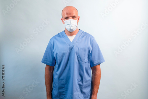 Portrait of a physiotherapist in light blue gown and face mask looking at camera in studio.