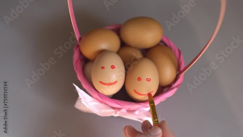 Close-up of a hand painting emojis with a brush on eggs. Easter tradition of painting eggs. Eggs in a basket are a symbol of Easter.