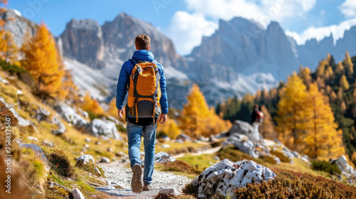 A man with a backpack walking along a trail that leads up a mountain in a scenic natural landscape