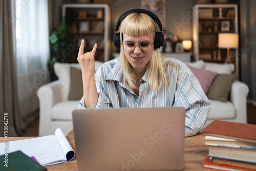 Young hipster university student woman listening heavy metal rock and roll or hard core music on wireless headphones using books and laptop for study and learning at home for educational exam