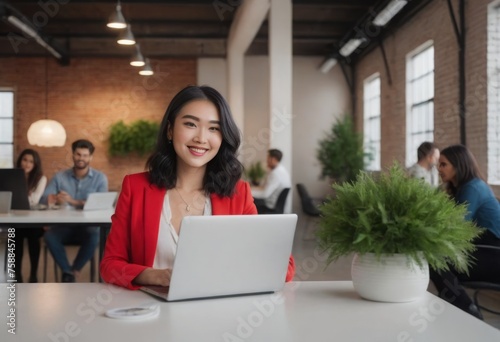 A focused young woman at her laptop in a modern workplace, colleagues in the background. She appears diligent and professional. photo