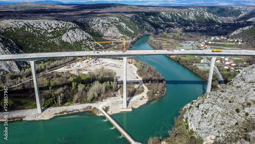 Construction of a high bridge over the river, aerial drone view. Workers and machines on construction site. Highway bridge.