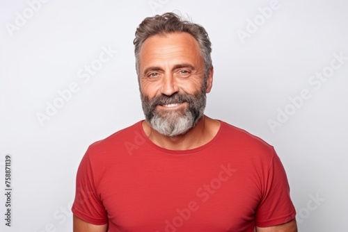 Portrait of handsome mature man in red t-shirt looking at camera and smiling while standing against grey background
