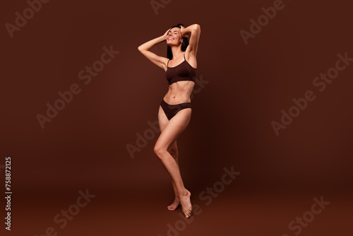 Unfiltered full length photo of sensual stunning girl with thin body hold hands on head wash hair isolated on dark brown color background